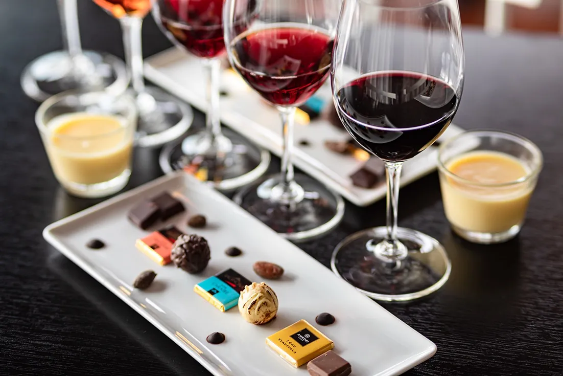 Glas med rödvin uppställda bakom rektangulära fat med pralin- och chokladbitar, redo för en vin- och chokladprovning.